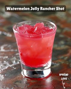 a red drink sitting on top of a table next to a glass with watermelon jolly rancher shot