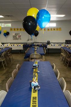 a table set up for a party with blue and yellow tablescloths, black and white balloons