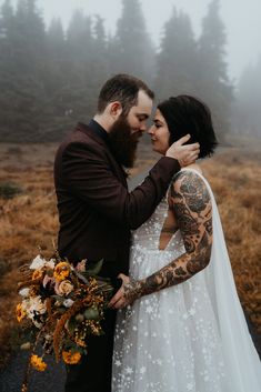 a tattooed bride and groom embracing each other in the middle of a foggy field