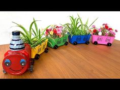 a toy train with plants in it sitting on a wooden table next to some flowers