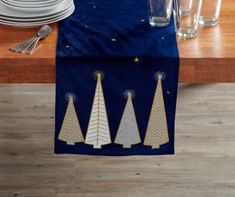 a blue table runner with three christmas trees on it and silverware in the background