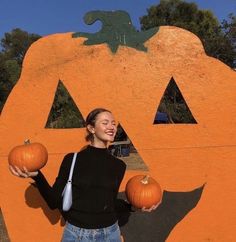 a woman holding two pumpkins in front of a carved pumpkin