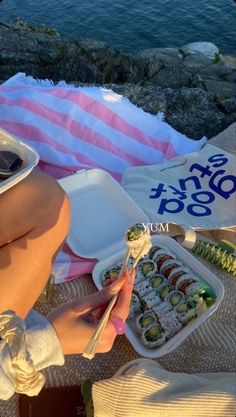 a woman eating sushi at the beach with chopsticks in front of her