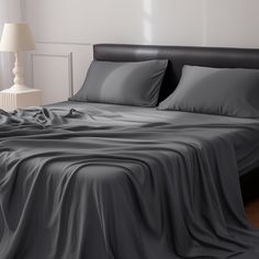 an unmade bed with grey sheets and two lamps on either side of the bed