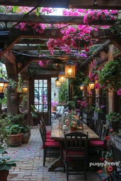 an outdoor dining area with pink flowers hanging from the ceiling and potted plants on the walls