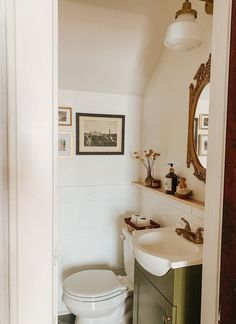 a white toilet sitting next to a sink in a bathroom under a framed painting on the wall