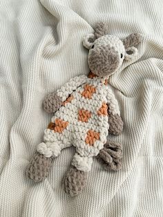 a crocheted giraffe laying on top of a white bed sheet with orange spots