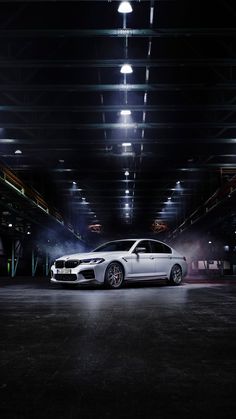 a white car is parked in an empty parking garage at night with lights on the ceiling