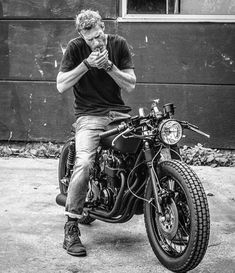 black and white photograph of man sitting on his motorcycle eating something out of his hand