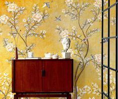 a cabinet with two cups on it in front of a wallpapered background that has flowers and birds