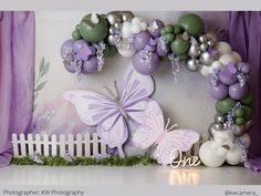 a purple and white backdrop with balloons, flowers and a butterfly in the center for a photo booth