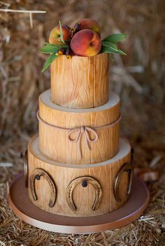 a three tiered wooden cake with fruit on top, sitting in the hay and straw