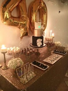 a table topped with lots of cake and desserts next to giant gold balloons in the background