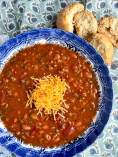 a blue and white bowl filled with chili next to two pieces of baguette bread