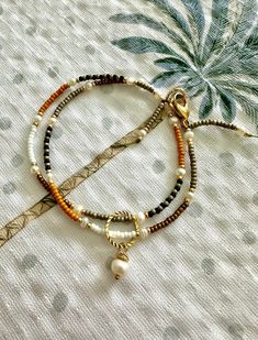 two bracelets with beads and charms on top of a white cloth covered tablecloth