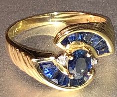 This lovely art deco revival 1970s-80s ring, is stamped 10K yellow gold, and boasts a lovely retro design with a center sapphire surrounded by channel set stones and a couple of little satellite diamonds. I believe the sapphires to be natural and untreated. The ring is about a size 7 and would be great as a birthstone ring or alternative engagement ring. Weighing approximately 2.7g total, it's in very good vintage condition with no damage or repair. Make sure to view all photos and zoom in for d Vintage Sapphire Ring With Accent Stones, Vintage Gold Sapphire Ring With Accent Stones, Vintage Gold Sapphire Ring With Emerald Cut, Gold Oval Sapphire Ring In Art Deco Style, Vintage Sapphire Rings Stamped 14k, Vintage 14k Stamped Sapphire Ring Collectible, Art Deco Gold Sapphire Ring In 14k Gold, Luxury Gold Art Deco Sapphire Ring, Art Deco Yellow Gold Sapphire Ring For Gift