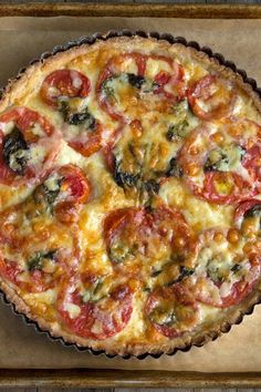 an overhead view of a pizza pie with tomatoes and spinach on top, sitting on a baking sheet