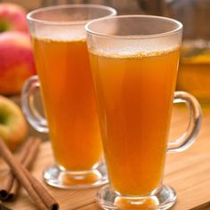 two glasses of apple cider on a tray with cinnamon sticks and apples in the background