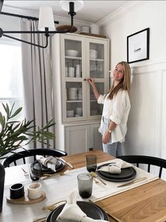 a woman standing in front of a table with plates and glasses on top of it