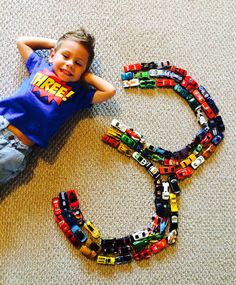 a young boy laying on the floor next to a toy car track that has cars all over it