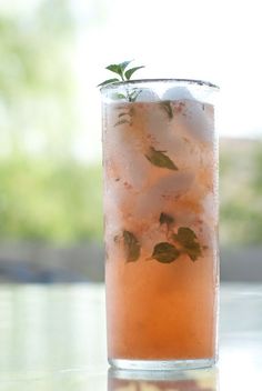 a tall glass filled with ice and mint sprigs on top of a table