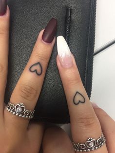 two fingers with hearts tattooed on them, one has a ring and the other has a heart