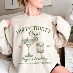 a woman wearing a dirty thirty crew sweatshirt in front of a bed with drinks on it