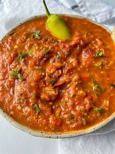 a white bowl filled with red sauce and a green pepper on top of the soup