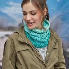 a woman wearing a green scarf and jacket looking at her cell phone while standing in front of a mountain backdrop