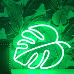 a neon sign that is lit up in front of a wall with leaves on it