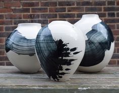 three black and white vases sitting on top of a wooden table next to a brick wall