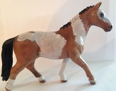 a toy horse with white and brown spots on it's body, standing in front of a white background