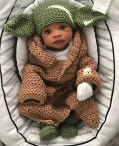 a baby in a crocheted yoda outfit laying on top of a blanket