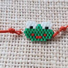 a piece of bead art on a white cloth with red string and green beads