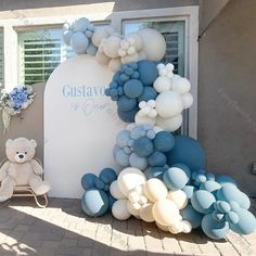 a teddy bear sitting in front of a balloon arch with blue and white balloons on it