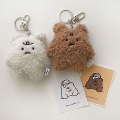 two small stuffed animals are sitting next to each other on a white surface, one is wearing a hat and the other has a sticker