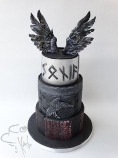 a three tiered cake decorated with black and white icing, wings and letters