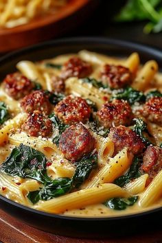 pasta with meatballs and spinach in a bowl on a wooden table next to other dishes