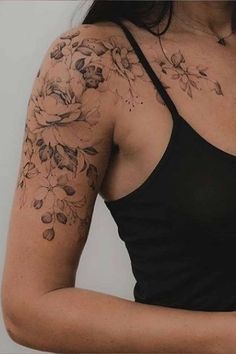 a woman wearing a black tank top with flowers on her arm and shoulder tattoo design