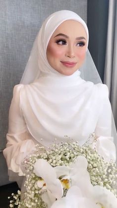 a woman wearing a white hijab and holding a bouquet of flowers in her hands