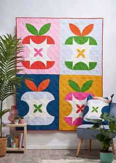 a colorful quilt hanging on the wall next to a blue chair and potted plant