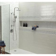 a bathroom with white tile and black dots on the shower wall, along with two shelves