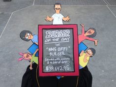 a chalkboard with cartoon characters on it in front of a parking lot that says burger of the day