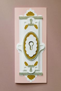 a white and gold card with a keyhole on the front that is attached to a pink background