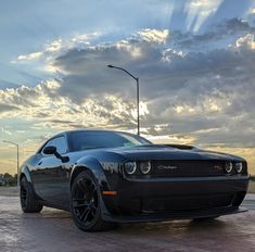 a black sports car parked in front of a parking lot at sunset with clouds overhead