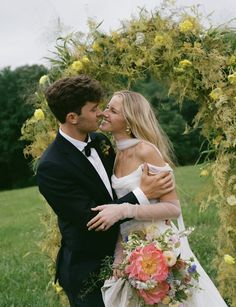 a bride and groom embracing each other in front of an arch with flowers on it