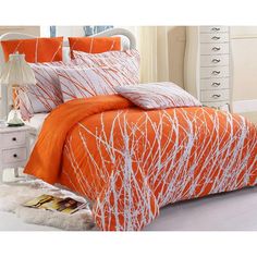 an orange and white comforter set with branches on the bed in front of a window