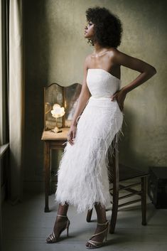 a woman in a white dress standing next to a chair