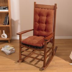 a wooden rocking chair with an orange cushion on the seat and bookshelf in the background