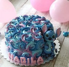 a blue and pink cake sitting on top of a wooden table next to some balloons